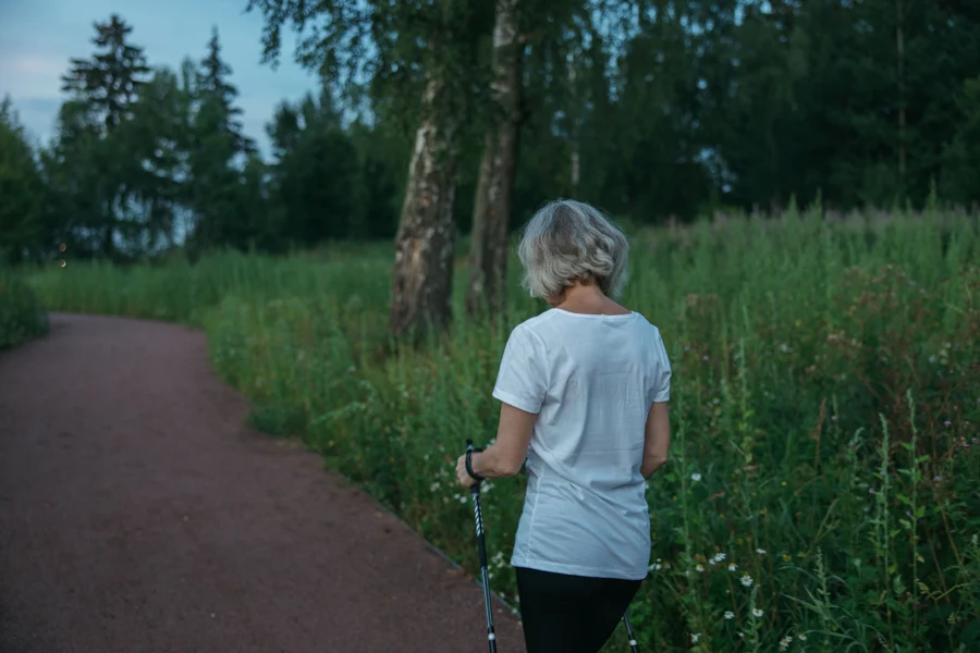 Femme âgée marchant avec des bâtons sur un chemin en bordure de parc