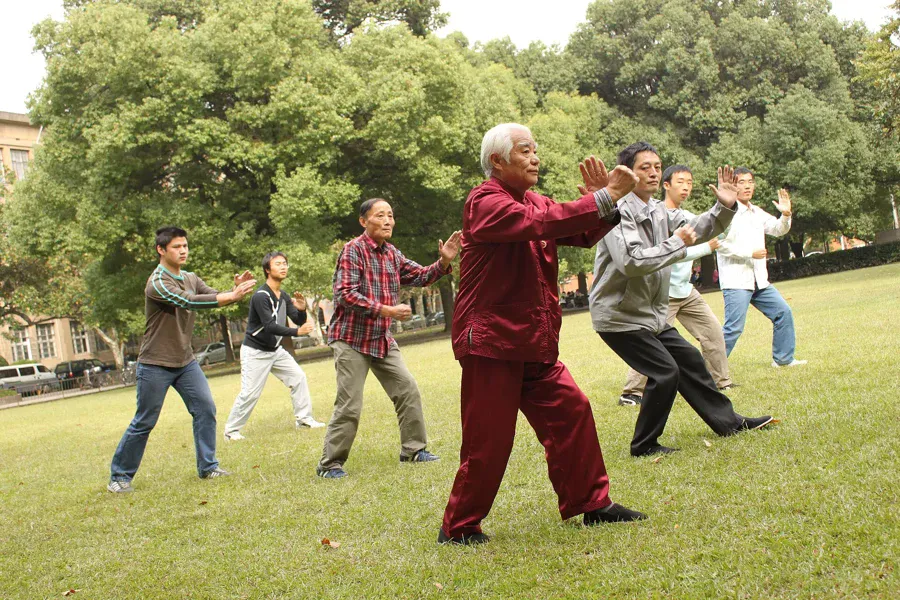 Groupe de pratiquants de tai chi en plein air, bras levés, genoux fléchis
