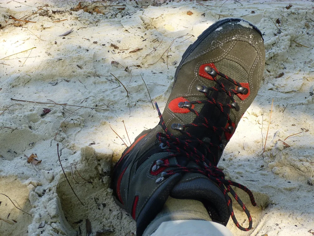Chaussure de randonnée lacée au pied, posée dans le sable, avec une chaussette qui dépasse